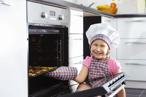 Cute little girl put cookies in stove — Zdjęcie stockowe