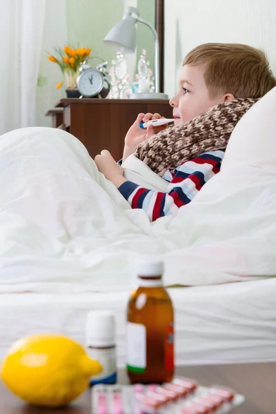 Sjuk liten pojke ligger i sängen med termometer — Stockfoto