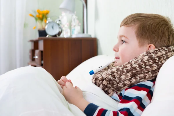 Sjuk liten pojke ligger i sängen med termometer — Stockfoto