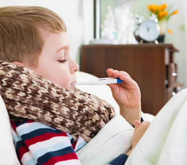 Sjuk liten pojke ligger i sängen med termometer — Stockfoto