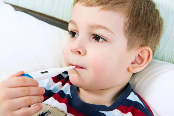 Sjuk liten pojke ligger i sängen med termometer — Stockfoto