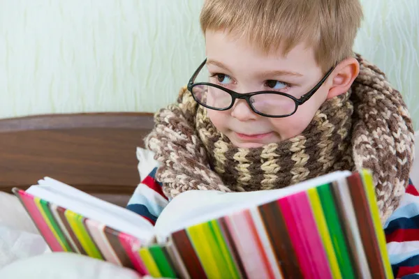Lite sjuk pojke läser bok i sängen — Stockfoto