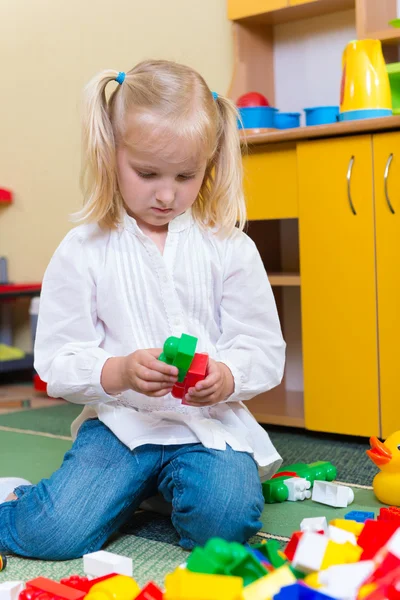 Piccola ragazza bionda che gioca con mattoni da costruzione nella scuola materna — Foto Stock