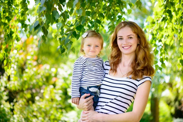 Schöne junge Mutter und süße Tochter lächeln der Natur zu — Stockfoto