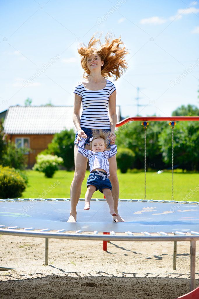 Young mother and little daughter bouncing on trampoline