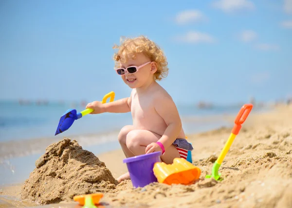 Menina bonito em óculos de sol brincando com areia — Fotografia de Stock