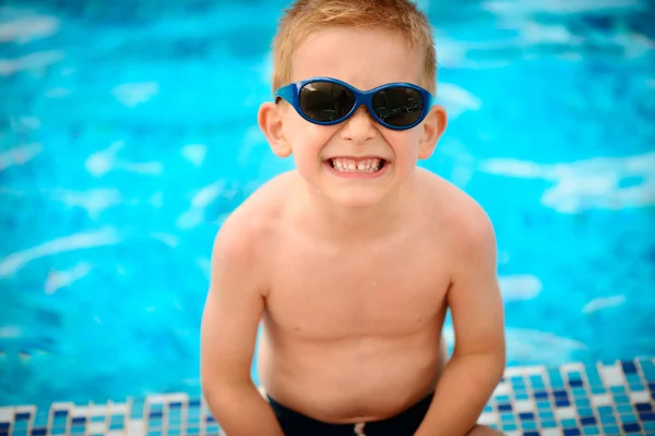 Garoto bonito em óculos de sol sentado na piscina — Fotografia de Stock