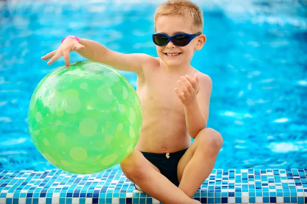 Garoto bonito em óculos de sol sentado na piscina — Fotografia de Stock