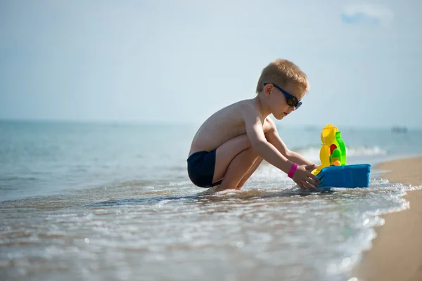 Мальчик в солнечных очках играет с игрушечной лодкой — стоковое фото