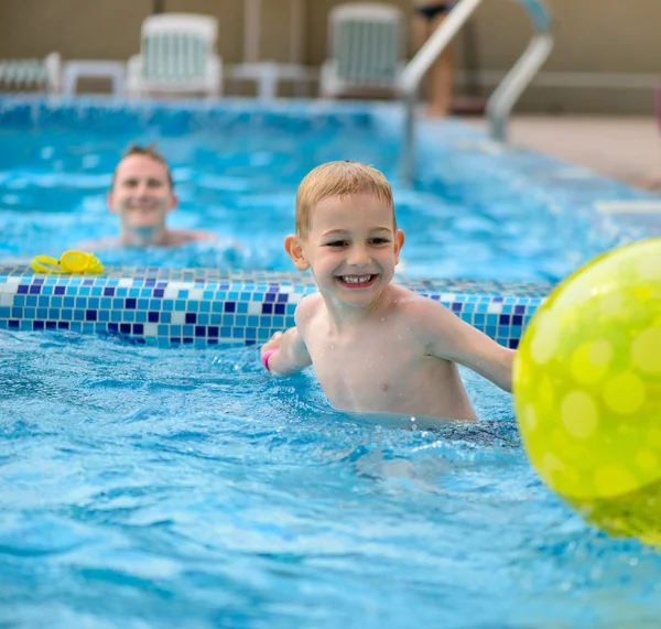 Feliz pai e filho brincando com bola na piscina — Fotografia de Stock