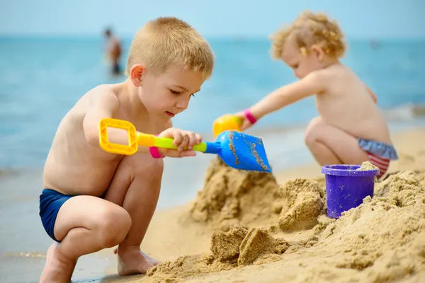 Two children playing with sand at ocean beach — Stock Photo, Image