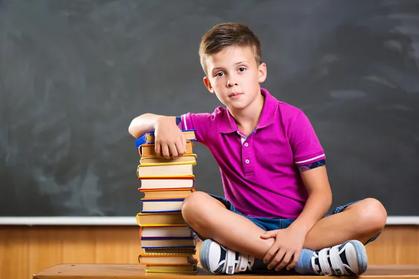 Mignon écolier assis avec livres dans salle de classe — Photo