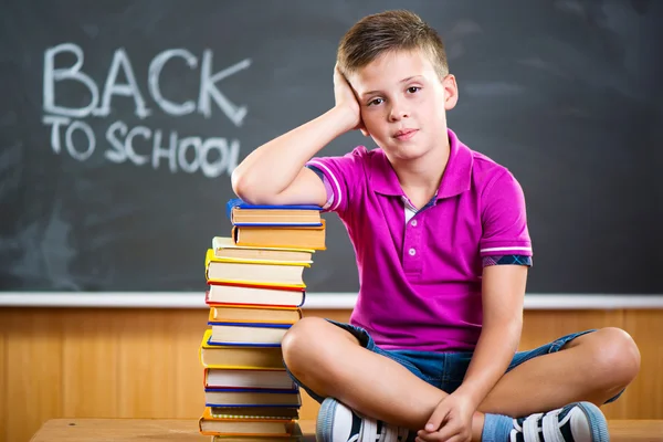 Cute school boy sitting with books in classroom — Stock Photo, Image