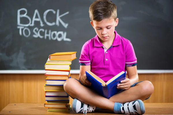 Cute school boy reading book in classroom — Stock Photo, Image