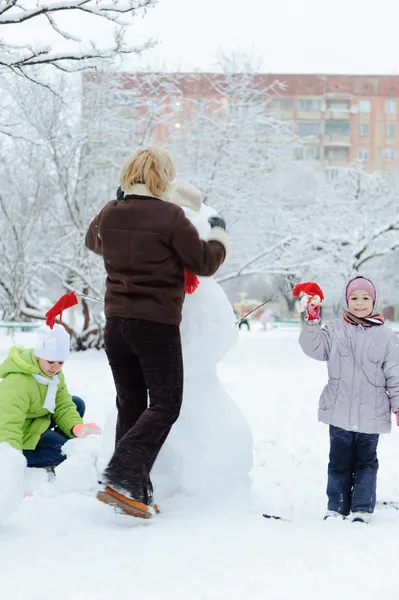 Moeder en kinderen gebouw sneeuwpop — Stockfoto