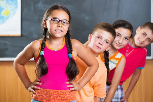 Quatre écoliers debout en classe contre le tableau noir — Photo