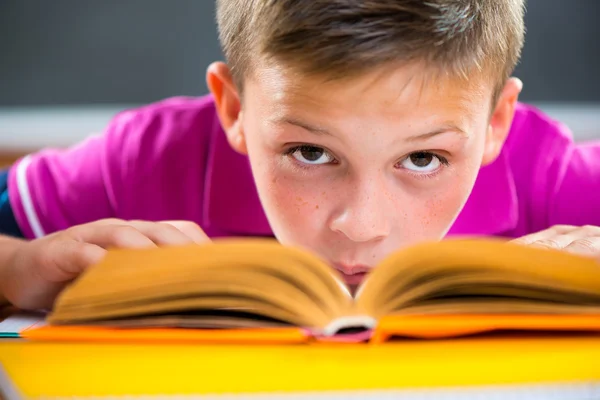 Cute schoolboy reading in classroom — Stock Photo, Image