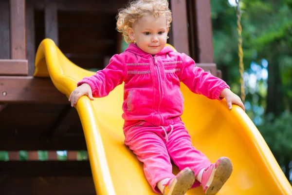 Gekrulde blond meisje glijden op speelplaats — Stockfoto