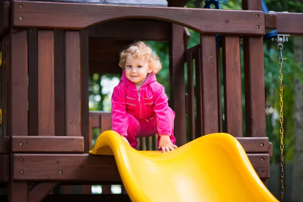 Curly menina loira deslizando no parque infantil — Fotografia de Stock