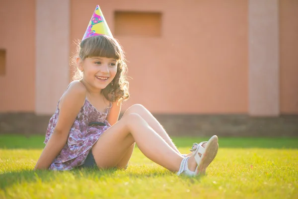 Glückliches Mädchen sitzt auf grünem Gras bei Geburtstagsparty — Stockfoto