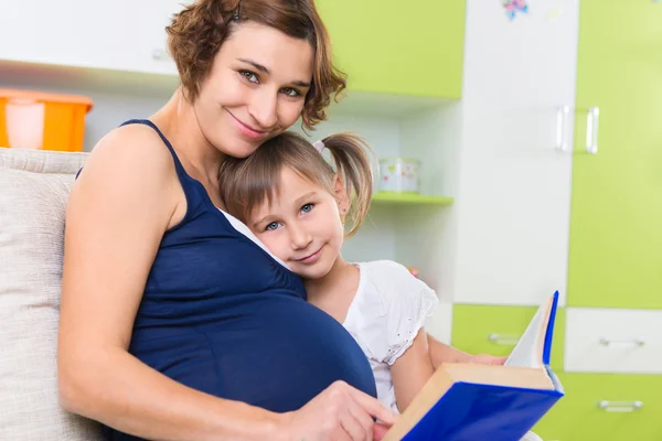 Pregnant mother with her daughter reading book — Stock Photo, Image