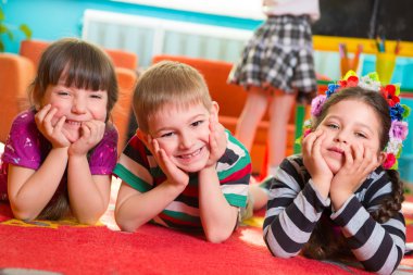 Üç çocuk altında yanaklarını elleriyle yerde yatarken