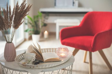 Siyah koffi, koyu çikolata ve bir kitapla süslü beyaz tepsi fotoğrafı. Arka planda rahat bir sandalye