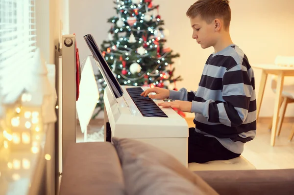 打网球的男孩在家里练习弹奏钢琴 伴奏的是新年树 — 图库照片