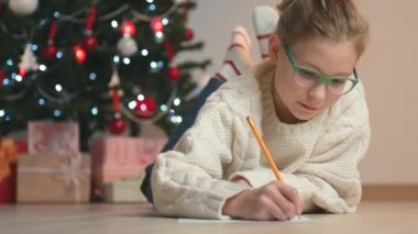 Noel ağacının altına Noel Baba 'ya mektup yazan güzel bir genç kızın portresi.