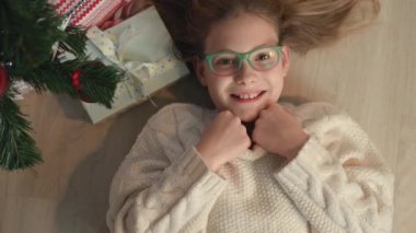 Noel ağacının altında yeni yıl hediyeleriyle yerde yatan küçük tatlı bir kızın 4k portresi. 