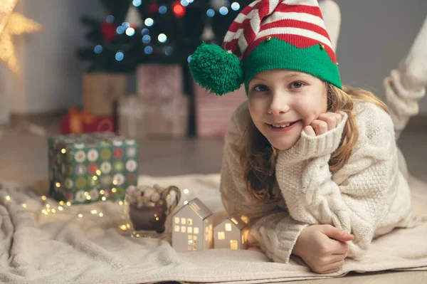 Linda Niña Con Sombrero Divertido Sentado Cerca Del Árbol Navidad Imagen de archivo