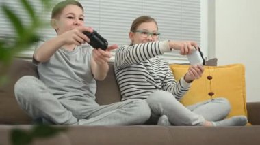 Mutlu ergen kardeşler. Çocuklar video oyunu oynuyor ve birlikte eğleniyorlar. Oturma odasında kanepede oturuyorlar.