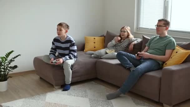 幸せな若いですお父さんともに笑顔と満足の子供たちは リビングルームでソファの上にコントローラーでコンピュータゲームをプレイ — ストック動画
