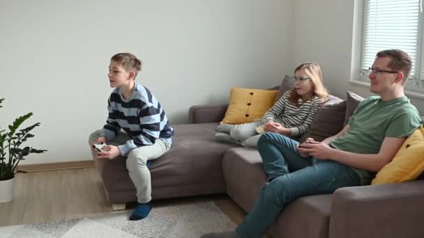 幸せな子供たちはコンピュータゲームをプレイし 父親と一緒に家のリビングルームでソファに座って楽しんでいます — ストック動画