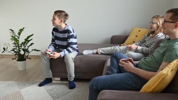 快乐的孩子们玩电脑游戏 和爸爸坐在客厅的沙发上玩得开心 — 图库视频影像