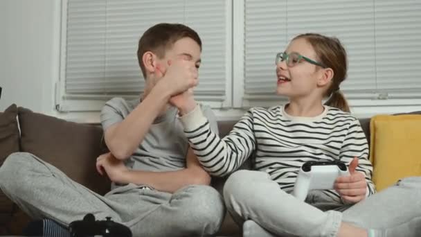 快乐的少年兄弟姐妹孩子们一起玩电子游戏 一起坐在客厅的沙发上玩乐 — 图库视频影像