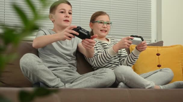 快乐的少年兄弟姐妹孩子们一起玩电子游戏 一起坐在客厅的沙发上玩乐 — 图库视频影像
