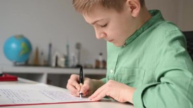 Genç okul çocuğu evde ödev yapıyor ve eski moda mürekkep kalemleriyle deftere yazıyor.