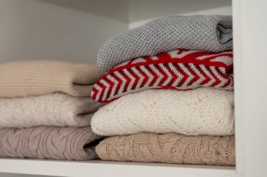 Dolabın rafında düzgünce katlanmış renkli kıyafetlerin yakın plan fotoğrafı.