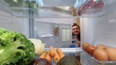 Genç bir kadın buzdolabını açıyor. İçeriden görüntüle.