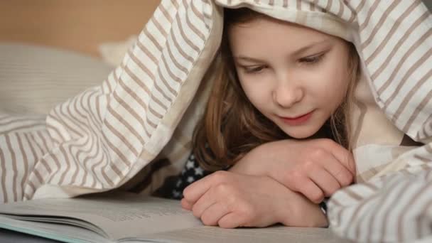 Küçük Tatlı Bir Kız Çocuğu Battaniyenin Altında Yatıp Kitap Okuyor — Stok video