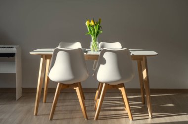 Beyaz minimalist iç mimarisi olan mutfak. Masada vazoda taze çiçekler var.