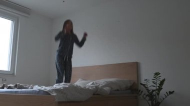 Mutlu genç kız pijamayla yatakta zıplıyor ve eğleniyor 