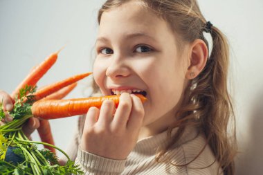 Tatlı genç kız taze turuncu havucu ısırıyor. Yüze yakın çekim