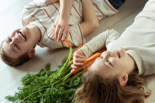 Laughing Teen Brother Sister Lying Floor Fresh Orange Carrots Hands — Stock Photo, Image