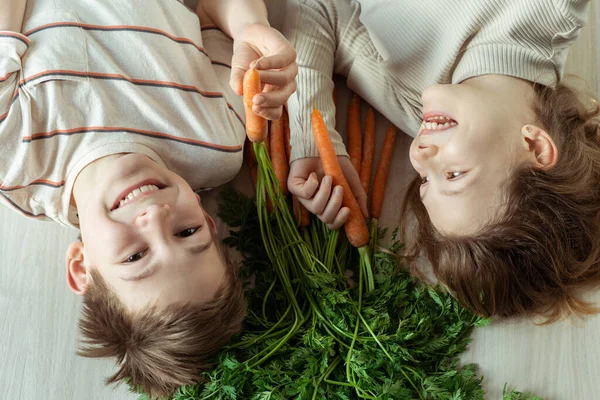Смеющиеся Младшие Брат Сестра Лежат Полу Свежей Апельсиновой Морковкой Руках — стоковое фото