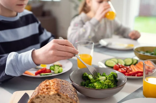 朝食をとる子供 オレンジジュースを飲んで フォークの上に新鮮な緑のブロッコリーをかじる — ストック写真