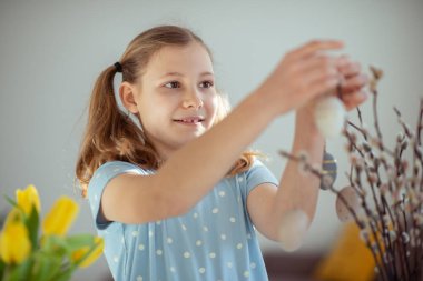 Mutlu genç kız evdeki ağaç dallarına paskalya yumurtası asıyor.