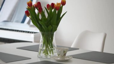 Masada vazoda güzel kırmızı ve sarı laleler ve modern oturma odasında kahve fincanı.