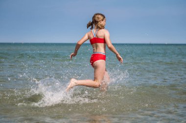 Happy teen child girl running and splashing water in turquoise sea at summer holidays